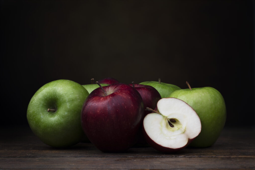 Group of red and green apples on rustic wooden surface with dark background and copy space